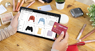 Person shopping online using a tablet and credit card on a workspace desk.