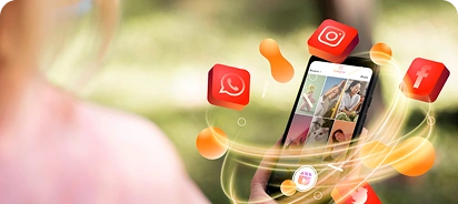 A woman's hand holding a smartphone displaying a photo gallery with images of people, surrounded by floating orange blob effects and 3D social media app icons (red WhatsApp, pink Instagram, red Facebook) in an outdoor green blurred background.