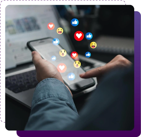 A person holding a smartphone with their finger touching the screen, while colorful social media reaction icons (likes, hearts, laughing emojis, thumbs up) float upward from the phone in front of a blurred laptop background.